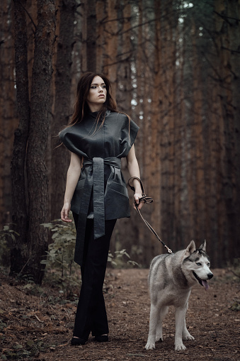 Female portrait of woman outdoors in the forest with wild dog together. Fairy tale atmosphere in dark. Fashion people. Woodland dweller in the nature. Friendship of human and animal like a wolf