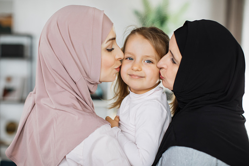 Little cute girl, her attractive young muslim mother and charming grandmother are spending time together at home. Women's generation. Happy International Women's Day