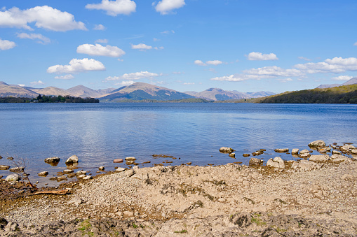 Sandstone rocks form a small beach on the shore of Loch Lomond on a bright, hazy, spring morning.