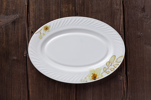 Simple white oval empty dish with ornaments on wooden old table, top view