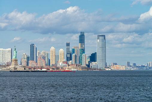 Panoramic view of the New Jersey coast and urban skyline from a ferry boat on the Hudson River, New York, USA. The Statue of Liberty in the foreground.