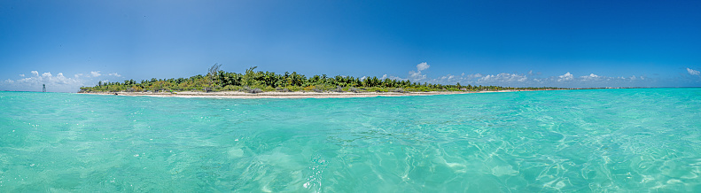 Panorama over a tropical beach taken from the water during the day with sunshine and blue sky