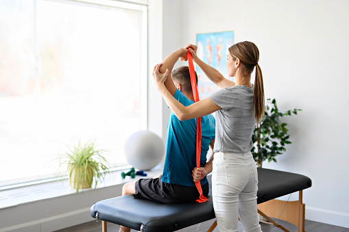 A Modern rehabilitation physiotherapy woman worker with man client using red elastic