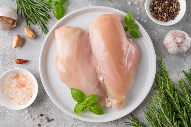 poitrine ou filet de poulet cru avec du sel, du poivre et des herbes fraîches sur une assiette blanche sur fond gris. aliments sains. vue de dessus, espace de copie. - chicken breast photos et images de collection