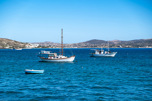 Wooden fishing boat moored in open Aegean calm sea, building, nature, clear blue sky background. Milos Greek island, Cyclades. Destination Greece, summer day.