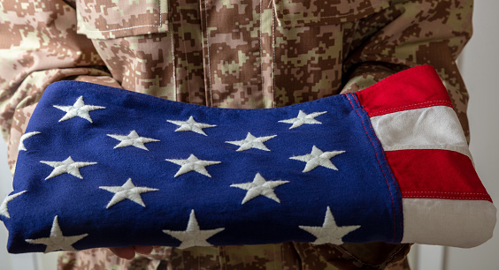 American army soldier in USA military digital pattern uniform, holds fold flag. United States, July 4th, independence day, camo uniform, US freedom.