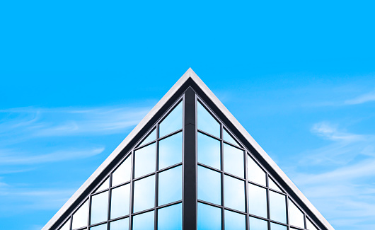 Symmetry and low angle view of glass office building in industrial loft style against blue sky background