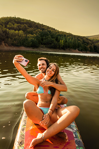 Couple taking selfies while paddle boarding at sunset