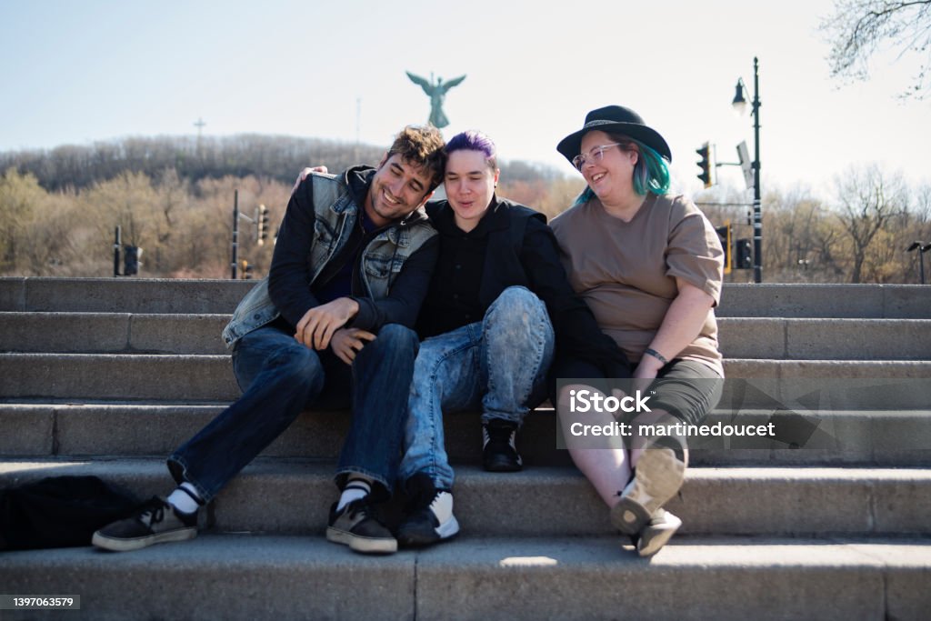 Group of LBGTQIA friends enjoying springtime in city public park. Group of LBGTQIA friends enjoying springtime in public city park sitting on staircase. They all have a unique hair style and are in their early thirties. The two women are a couple. Horizontal full length outdoors shot. Montréal Stock Photo