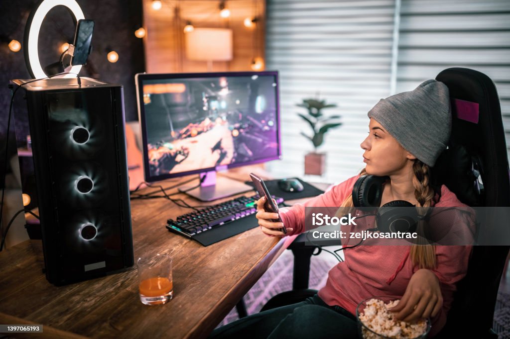 Gaming girl eating popcorn and looks at her phone girl eating popcorn and looks at her phone Desktop PC Stock Photo