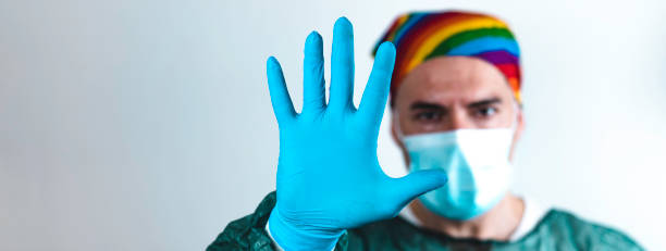 istock Horizontal banner or header with surgeon doctor with protective mask and rainbow bandanna on his head who is showing his hand in blue glove - Doctor stopping hiv virus or coronavirus with prevention 1397066114