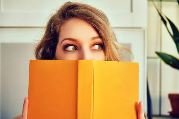 Photo of young woman covering face with book