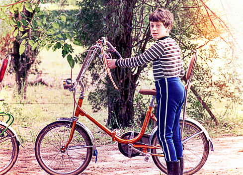 Vintage image of a boy with a bike standing outdoors.