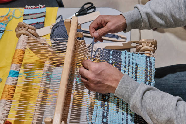 istock Hands of senior man weaving small rug with pattern on manual table loom. 1397068780