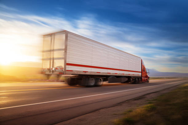 Red and white 16 wheeler with cargo speeding at sunrise on a single lane road USA stock photo