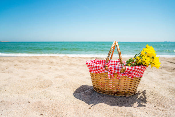 Picnic basket with yellow flowers on sand by the beach. High resolution 42Mp outdoors digital capture taken with SONY A7rII and Zeiss Batis 40mm F2.0 CF lens