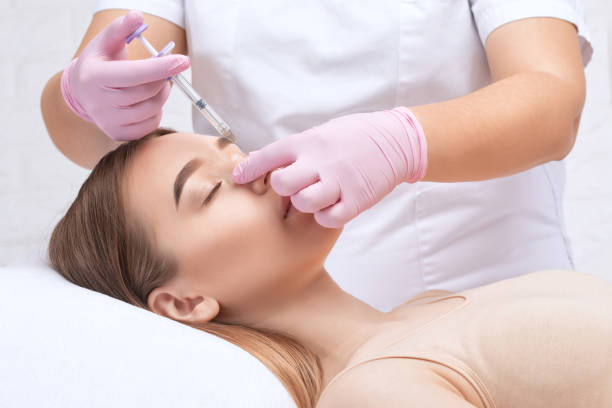 의사는 코의 고비를 교정하기 위해 주사를합니다. 미용사는 얼굴의 주름에 대한 주사를합니다. 뷰티 살롱에서 여성의 미용학. - plastic surgery botox injection face lift nose job 뉴스 사진 이미지