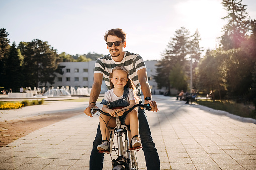 Happy father and his little toddler daughter rides a bike together