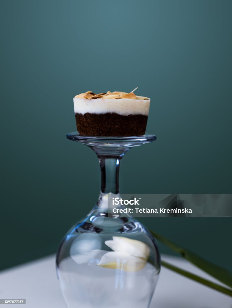 Keto fat bomb. Cake made from almond flour, dark chocolate with creamy coconut filling. Creative still life with upturned glass and tulip. Keto fat bomb. Cake made from almond flour, dark chocolate with creamy coconut filling. Creative still life with upturned glass and tulip on green blue background. Almond Stock Photo