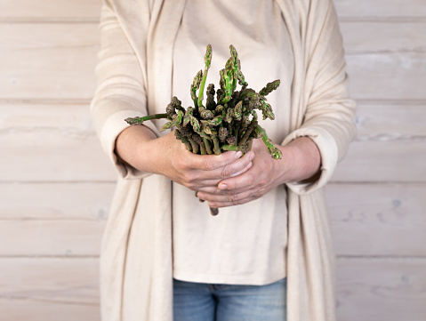 A woman holds a large bunch of fresh green asparagus in her hands. Healthy food and diet. Support for local business. Selective focus.