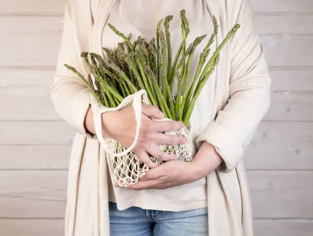 A woman holds a large bunch of fresh green asparagus in her hands. Healthy food and diet. Support for local business.