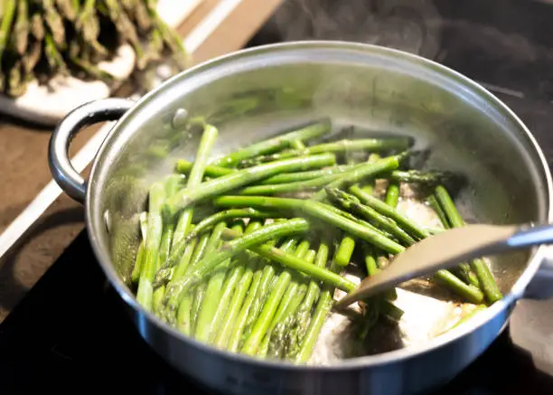 Cooking asparagus. Roasting green asparagus sprouts in a pan with butter and garlic. Healthy food and diet.