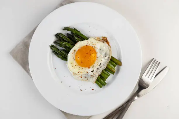 Cooking asparagus. Fried green asparagus sprouts and fried eggs on a white plate. Healthy food and diet.