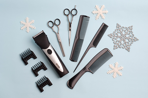 Hair clipper with attachments, regular and filler scissors, combs, snowflakes on a blue winter background. Concept: Winter, New Year discounts for hairdressing services, hairdressing tools.