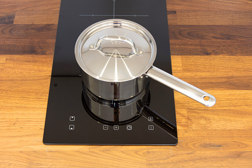 Saucepan ladle with lid on an induction hob built into a wooden kitchen worktop, top view