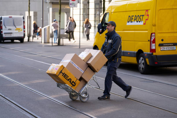 Postman with hand truck full of parcels at City of Zürich on a sunny spring morning. Shopping mile Bahnhofstrasse with delivering van of Swiss Post company. Photo taken March 21st, 2022, Zurich, Switzerland. street post stock pictures, royalty-free photos & images