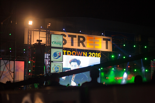 New year concert party stage in Bangkok at Ratchadaphisek Road 23. View over street and heads of people to stage and screen with banners outside of mall building The Street 23