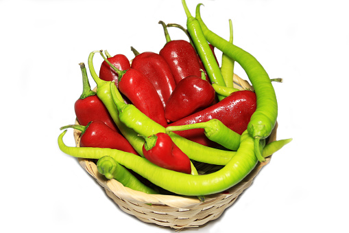 Freshly picked red and green peppers in wicker basket, isolated on white background