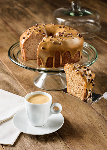 Delicious cake with chocolate chips topping, on a wooden table, with a coffee cup