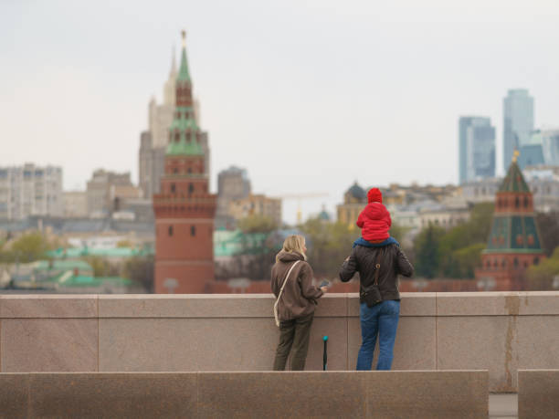 Moscow, Russia - May 2, 2022:  Cityscape in spring day. Red Kremlin Towers,  Moskva River, Bolshoy Kamenny Bridge, traffic, Stalinist architecture, modern MIBC. Family admire view