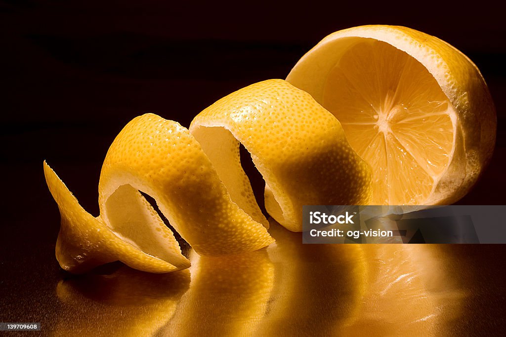 A half peeled lemon with the peel in a twist on a dark back Lemon with spiral peel Citrus Fruit Stock Photo