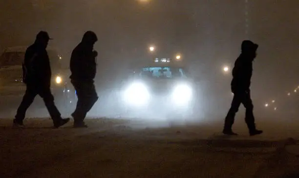 Three silhouetted people crossing the street at night caught in the headlights of a New York City taxi