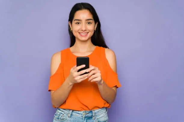 Smiling young woman texting her friends and family and posting on social media with her new smartphone