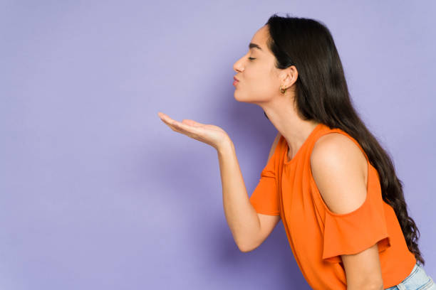 Loving attractive woman flirting Profile of an adorable young woman in love blowing a kiss to her partner or boyfriend against a studio background blowing a kiss stock pictures, royalty-free photos & images