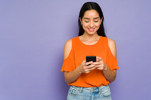 Happy hispanic woman using her smartphone while receiving and sending text messages to her partner and friends