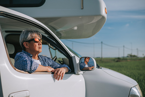 Asian chinese active senior man portrait leaning on campervan motor home door with cool attitude sunglasses looking away