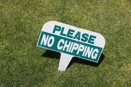 Green and white sign that says “Please No Chipping” at the golf course