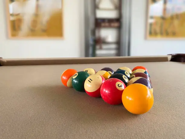 Colorful pool balls set up in triangle on beige felted billiards table. Background out of focus