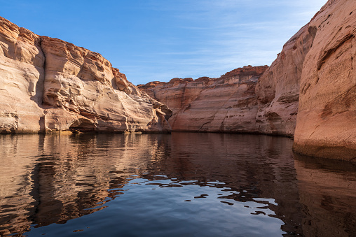 The smooth emerald water of the lake contrasts with the bright red terracotta sandstone shores. Lake Powell. USA. The coast is cut by narrow canyons.