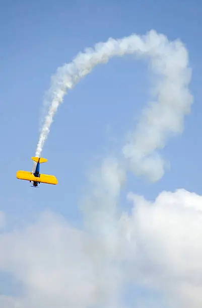Bi-plane against sky with curved smoke trail