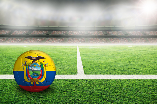 Football in brightly lit outdoor stadium with painted flag of Ecuador. Focus on foreground and soccer ball with shallow depth of field on background and copy space.