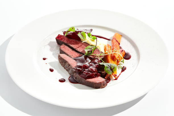 istock Venison steak with baked vegetables isolated on white plate. Meat steak medium rare roasted with carrot, beetroot and mashed potatoes with cherry sauce. Wild meat in restaurant menu. 1397135064