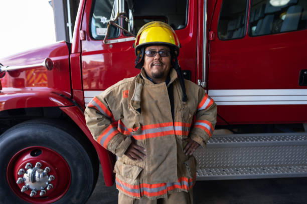 istock Cheerful Firefighter wearing protection suit standing in front of a fire engine truck 1397140884