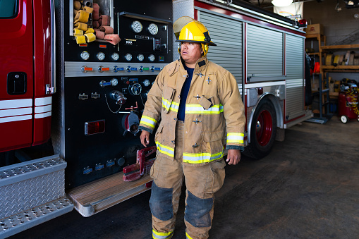 Indigenous Navajo Young Firefighter wearing protection suit approaching fire engine truck at the station
