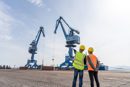 Male and female dock workers exchange work in front of port cranes