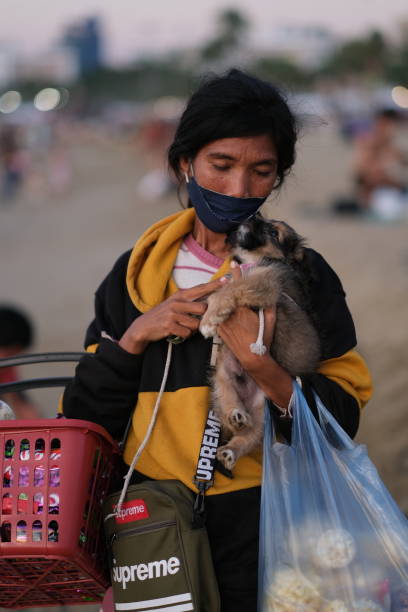 Poor woman is holding a puppy Pattaya, Chonburi Thailand - December 11 2021: Poor Asian woman is holding a puppy while selling snacks on the beach walking beach women sadness stock pictures, royalty-free photos & images